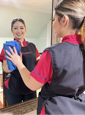 Housekeeper in uniform cleaning mirror with blue microfiber cloth in hotel or home setting - Cleaning in the DC Metro area.