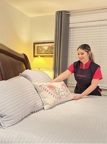 Hotel housekeeper making bed with fresh white linens in guest room - Cleaning in the DC Metro area.