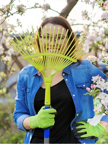 Person in blue jacket holding yellow garden rake in front of face during spring yard work with blooming trees - Cleaning in the DC Metro area.