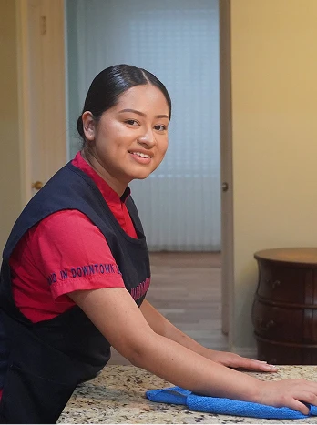 Professional house cleaner in uniform wiping kitchen counter with blue cloth, smiling at camera - Cleaning in the DC Metro area.