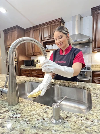Professional cleaner washing dishes at kitchen sink wearing gloves and apron in modern home - Cleaning in the DC Metro area.