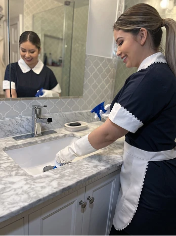 Housekeeper in uniform cleaning marble bathroom counter with mirror reflection - Cleaning in the DC Metro area.