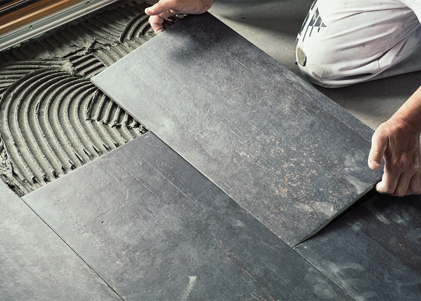 Professional tile installer laying large gray porcelain floor tiles with troweled adhesive mortar - Flooring installation in the DC Metro area.