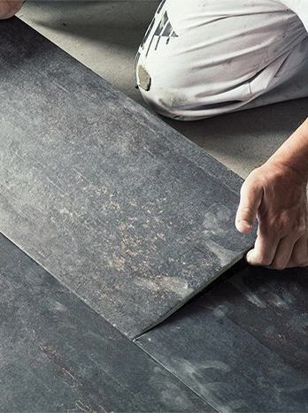Professional tile installer laying large gray porcelain floor tiles with troweled adhesive mortar - Flooring installation in the DC Metro area.