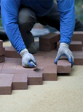 Worker installing red brick pavers in herringbone pattern on sand base for patio or walkway construction - Hardscaping in the DC Metro area.
