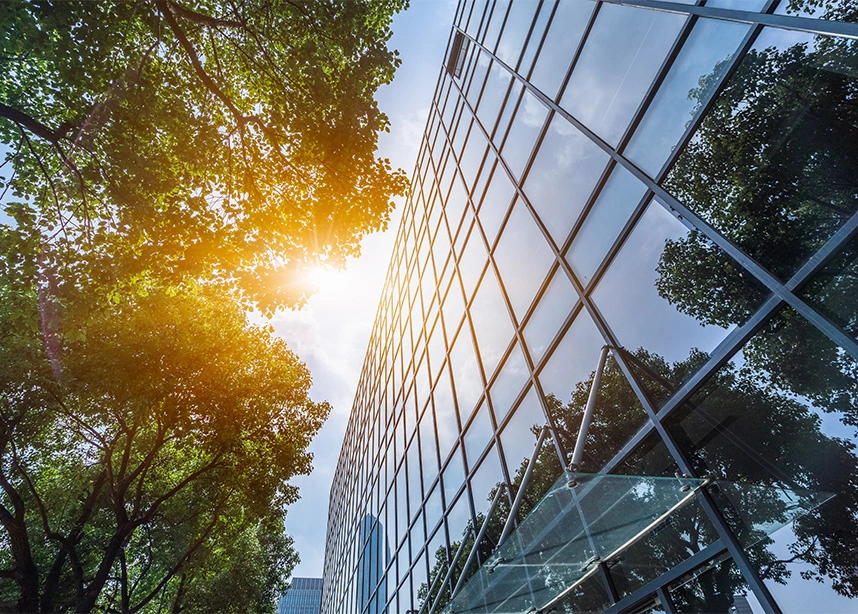 Modern glass office building exterior with green trees and sunlight reflecting off windows - Office cleaning in the DC Metro area.