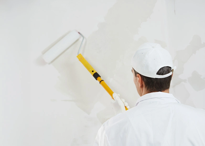 Painter in white uniform using yellow paint roller to apply white paint on interior wall - Painting in the DC Metro area.