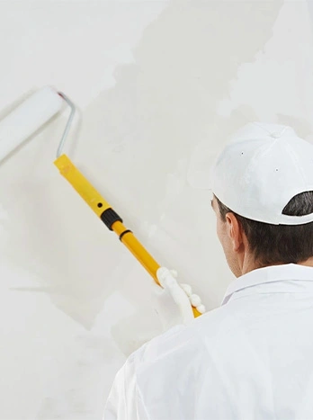 Painter in white uniform using yellow paint roller to apply white paint on interior wall - Painting in the DC Metro area.