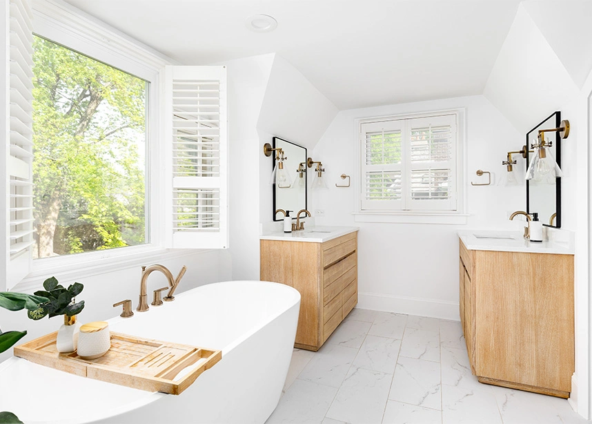 Bright modern bathroom with white freestanding tub, natural wood vanities, and large windows with greenery views - rental cleaning in the DC Metro area.