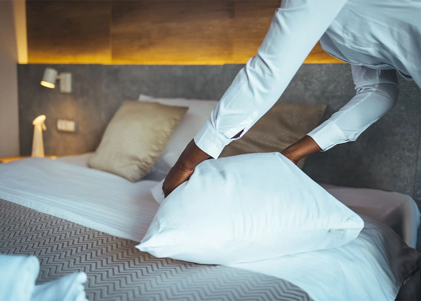 Person in white shirt arranging white pillows on hotel bed during professional cleaning service - First time cleaning in the DC Metro area.