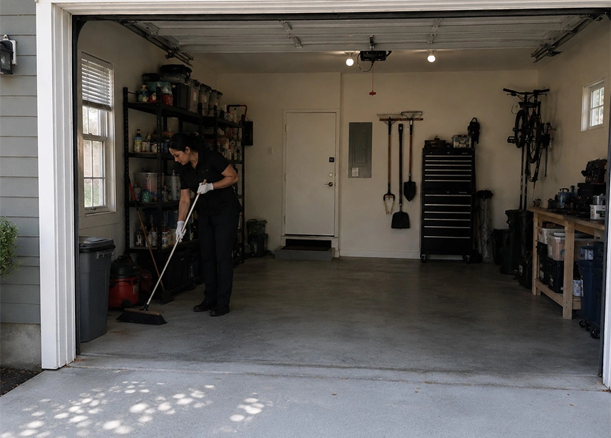 Person cleaning organized garage with broom, storage shelves and tools mounted on walls - Garage cleaning in the DC Metro area.