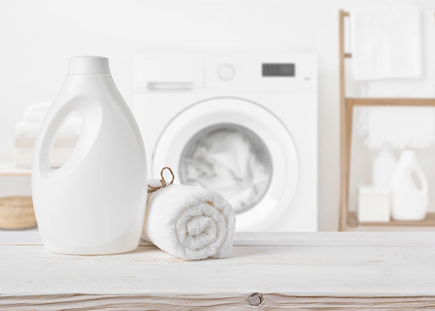 White laundry detergent bottle and rolled towel on counter with washing machine in modern laundry room - Laundry services in the DC Metro area.