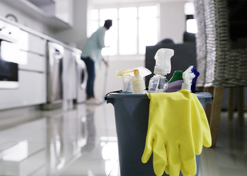 Cleaning supplies in bucket with yellow gloves on reflective floor while person cleans kitchen in background - Spring cleaning in the DC Metro area.